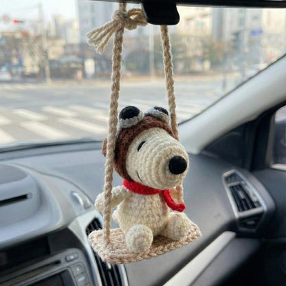 Crocheted dog toy on a swing hanging from a car's rearview mirror.