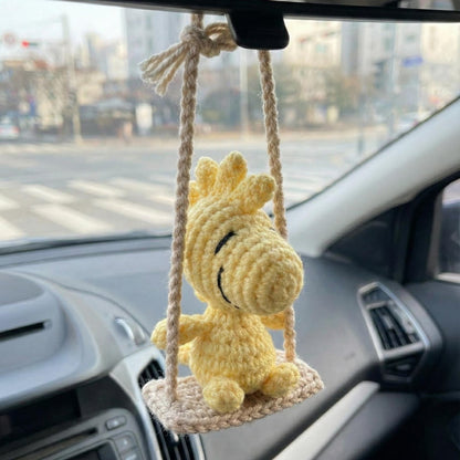 Yellow plush toy on a swing hanging from a car's rearview mirror.